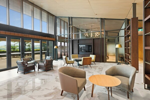 A spacious lobby with a high ceiling, large windows, and a modern seating area with sofas and a small table.