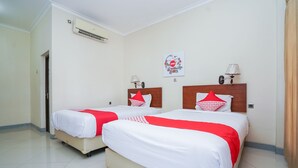Een hotelkamer met twee bedden, elk voorzien van wit beddengoed en rode accenten, een wandairconditioner, een decoratief wandpaneel en een bedlampje.