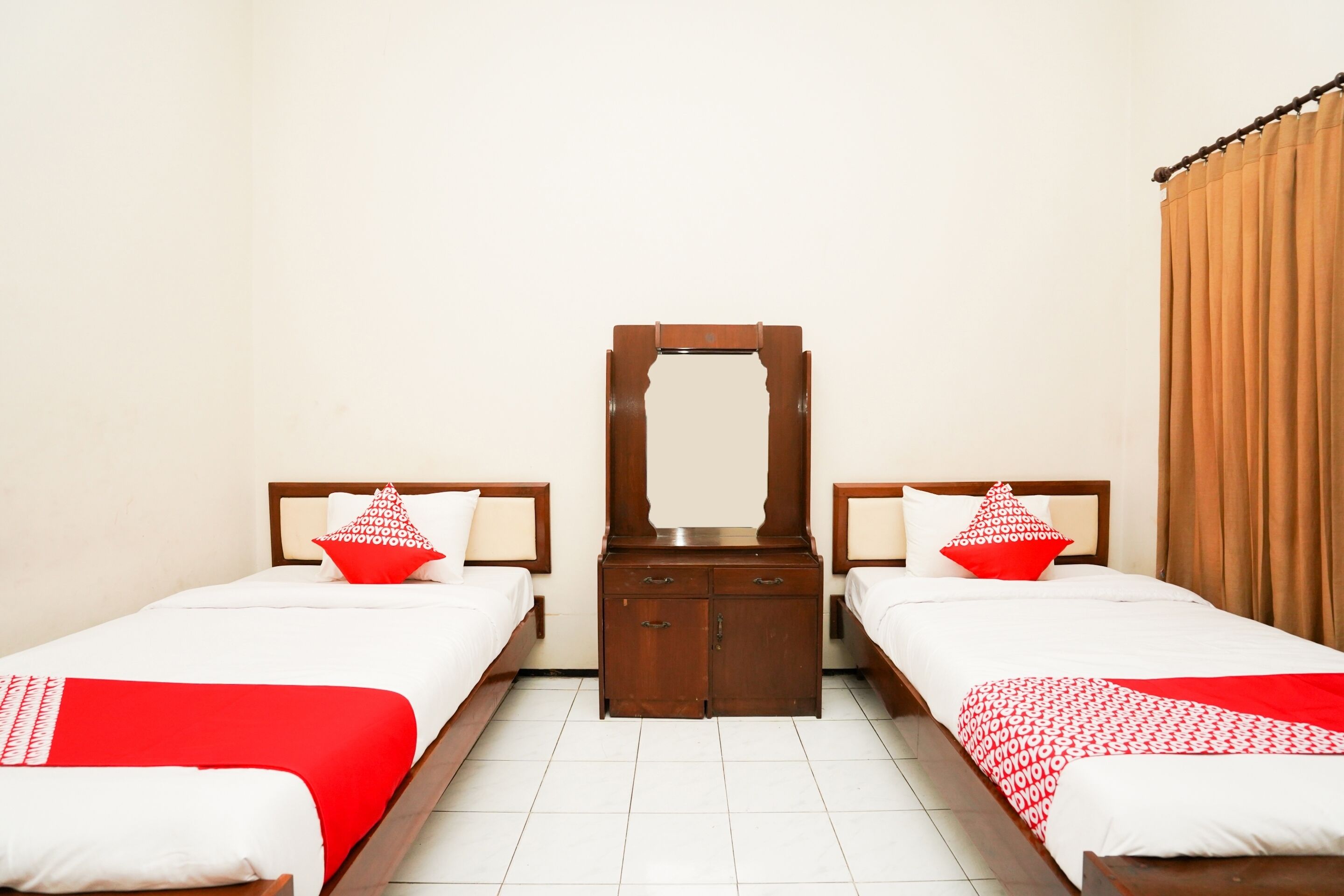A hotel room with two single beds, a wooden nightstand, a mirror, and a wooden wardrobe.