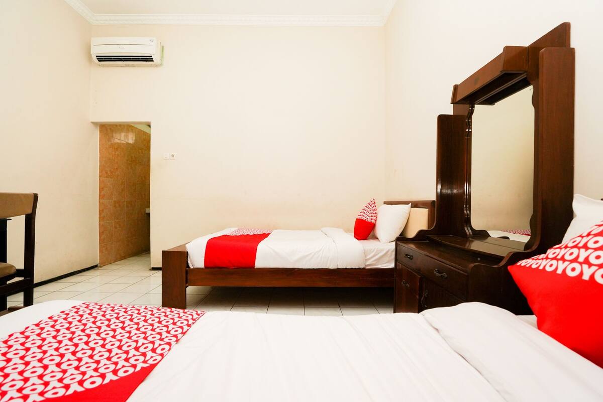 Een hotelkamer met een bed, een houten nachtkastje, een spiegel en een deur.