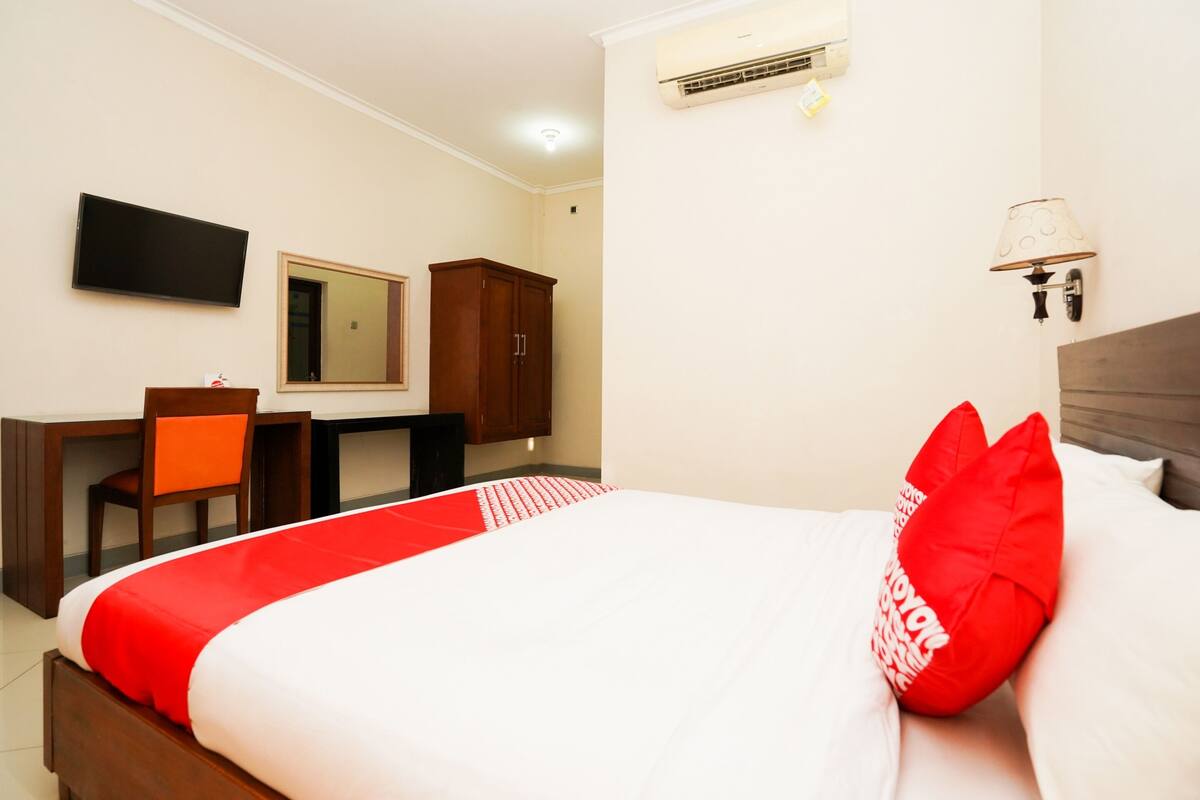 Hotelkamer met een bed, een bureau, een stoel, een spiegel, een airconditioner en een wandlamp.