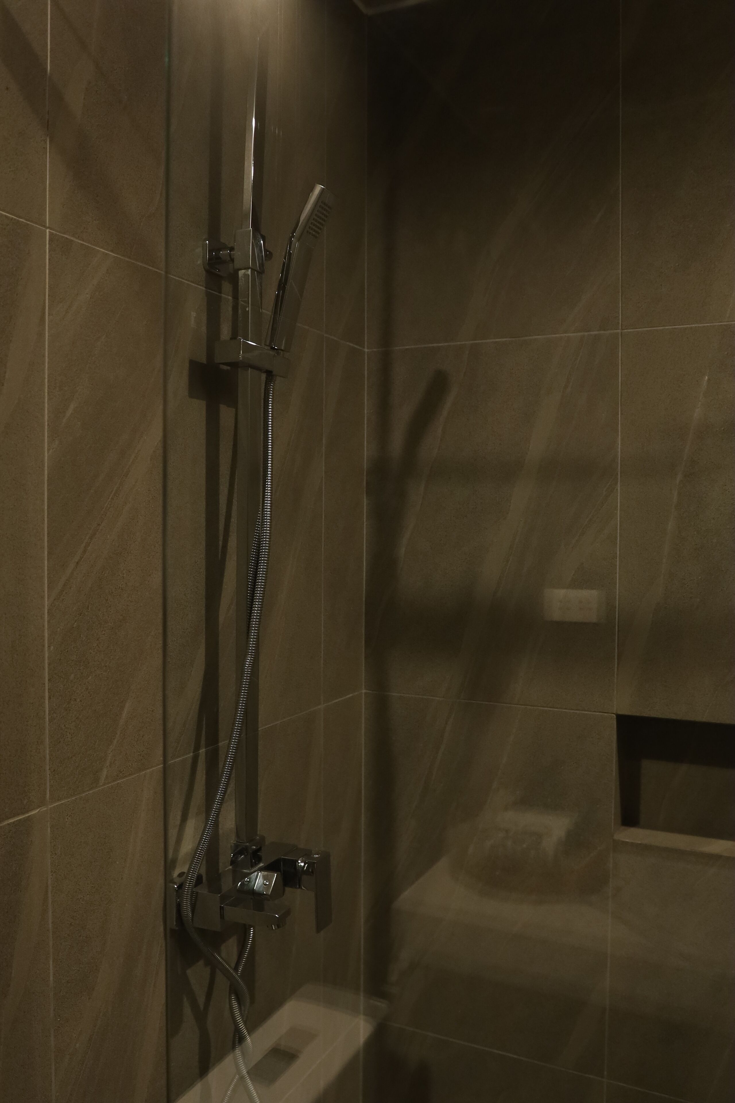 Un área de ducha con mampara de vidrio, un cabezal de ducha de mano y un grifo instalado en la pared.