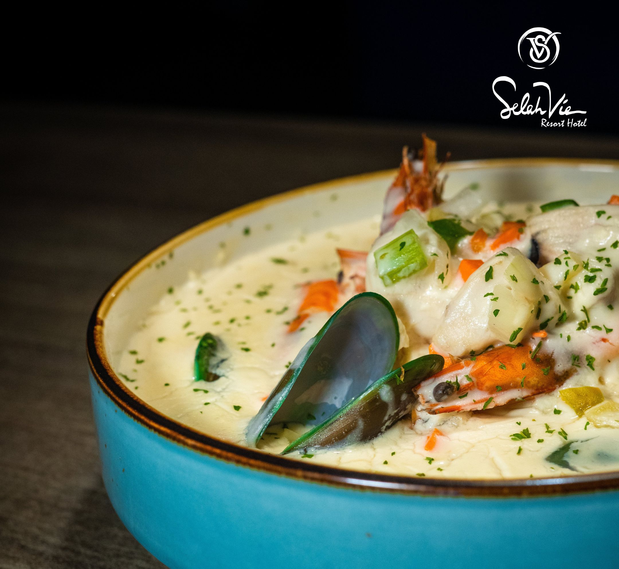 A bowl of seafood chowder with mussels and crab, served in a blue bowl.