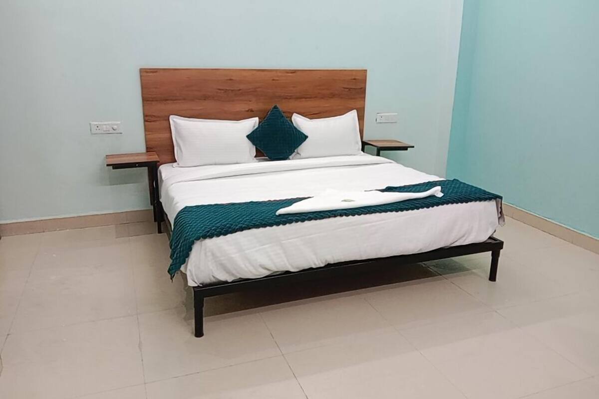 Ein ordentlich bezogenes Bett mit Holz-Kopfstück, weißer Bettwäsche und einer Türkis-Decke.