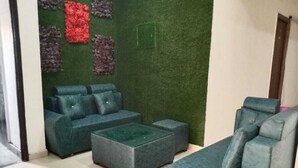 A living room with a green wall, a grey sofa, and a matching ottoman. - Hotel Soho Sector 51 Noida (Noida)