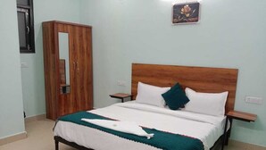 A single bed with a wooden headboard, white bedding, and a teal throw blanket. There is a wooden wardrobe to the left and a small table beside the bed. - Hotel Soho Sector 51 Noida (Noida)