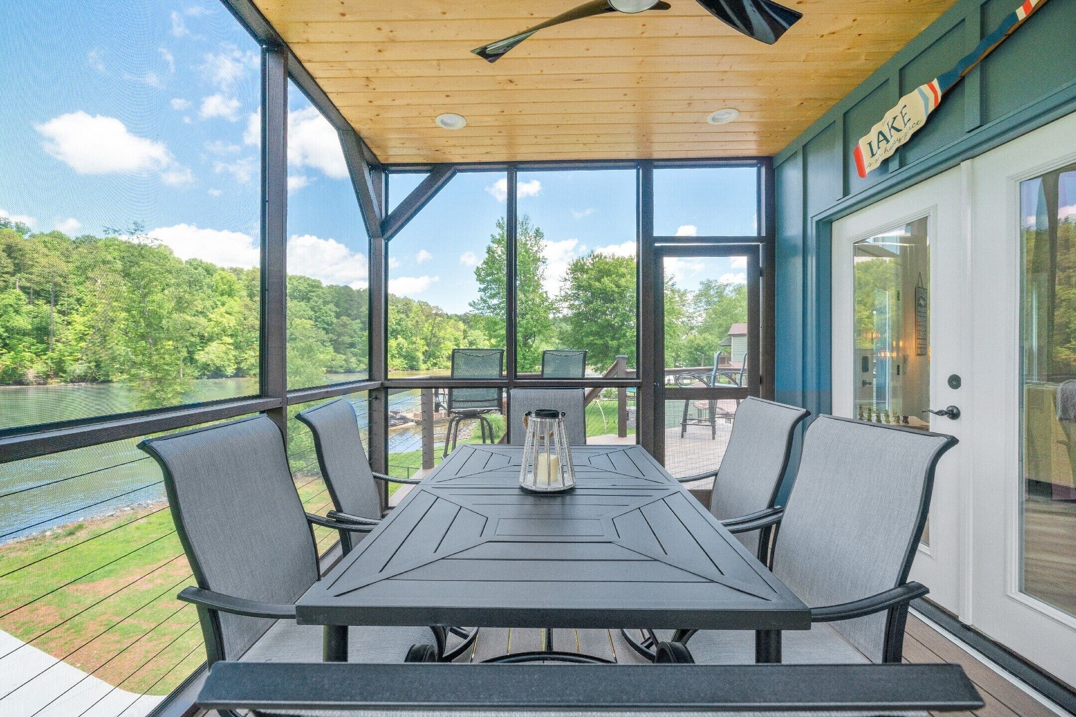 A covered outdoor dining area with a table and chairs, overlooking a body of water and greenery.