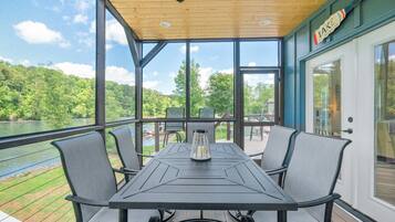 A covered outdoor dining area with a table and chairs, overlooking a body of water and greenery.