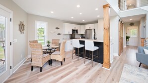 A modern kitchen with white cabinets, a central island, and a dining area with wicker chairs.
