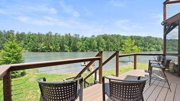 A deck with two wicker chairs overlooking a lake, surrounded by a wooden railing and a glass enclosure.