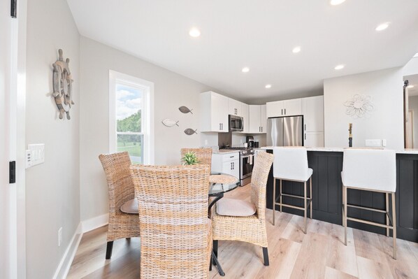 A modern kitchen with white cabinets, stainless steel appliances, and a black island. There are wicker chairs and a dining table.