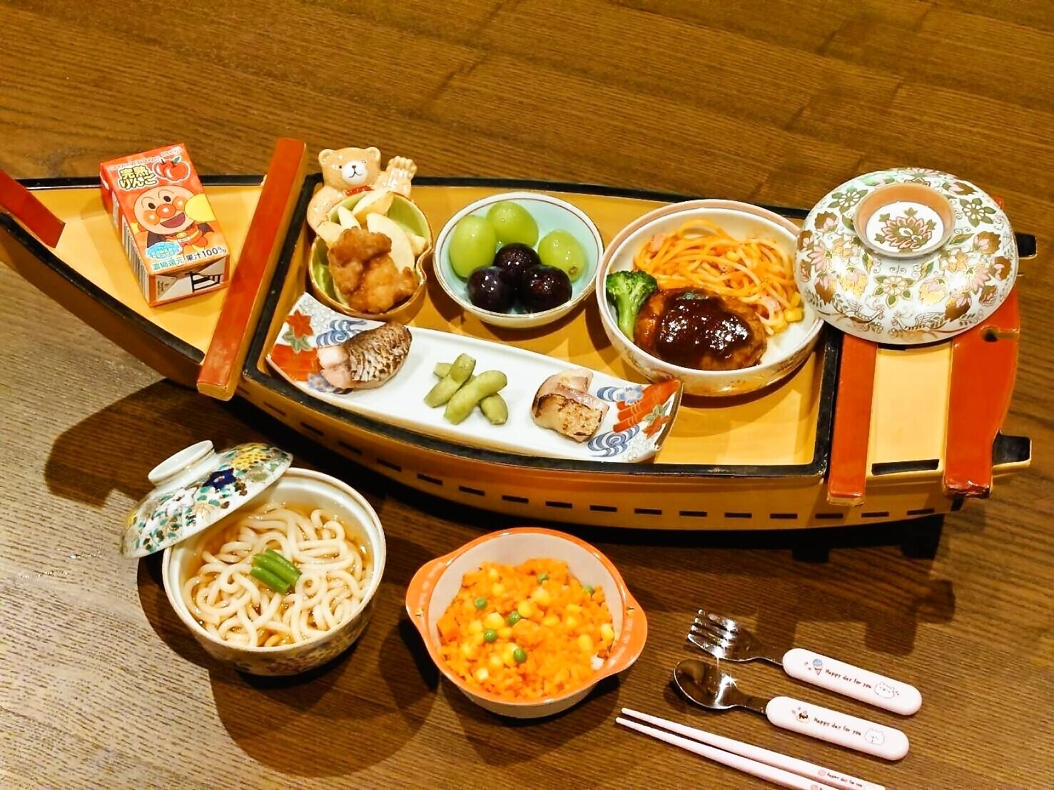 A traditional Japanese meal setup with various dishes including noodles, vegetables, and a small boat-shaped tray.