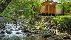 A traditional wooden building with a wooden deck overlooking a stream with rocks and greenery. - MIZUMARI (Kawazu)