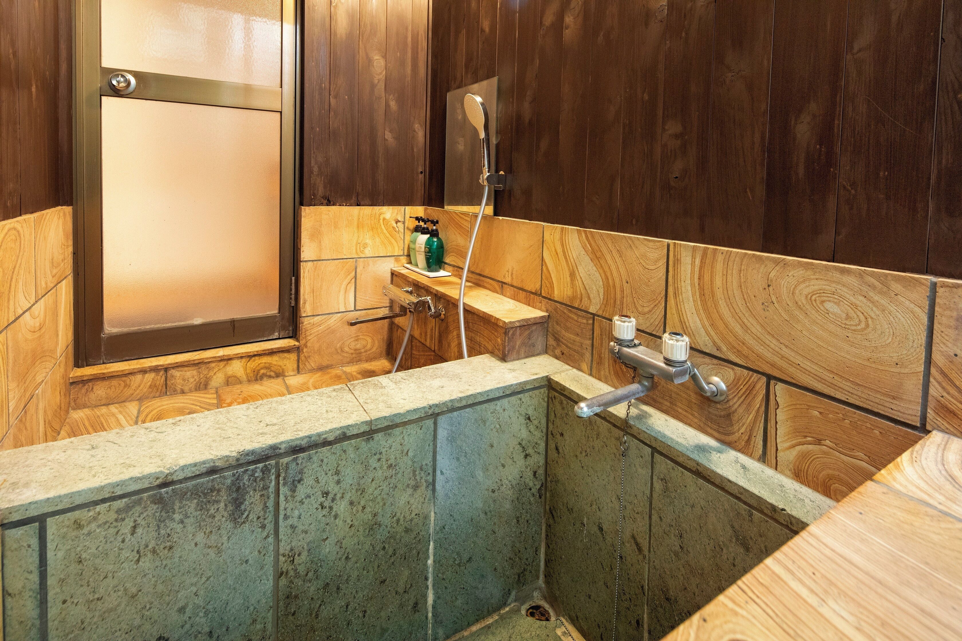 A bathroom with wooden walls, a glass shower enclosure, a wooden bench, and a small shelf with toiletries.