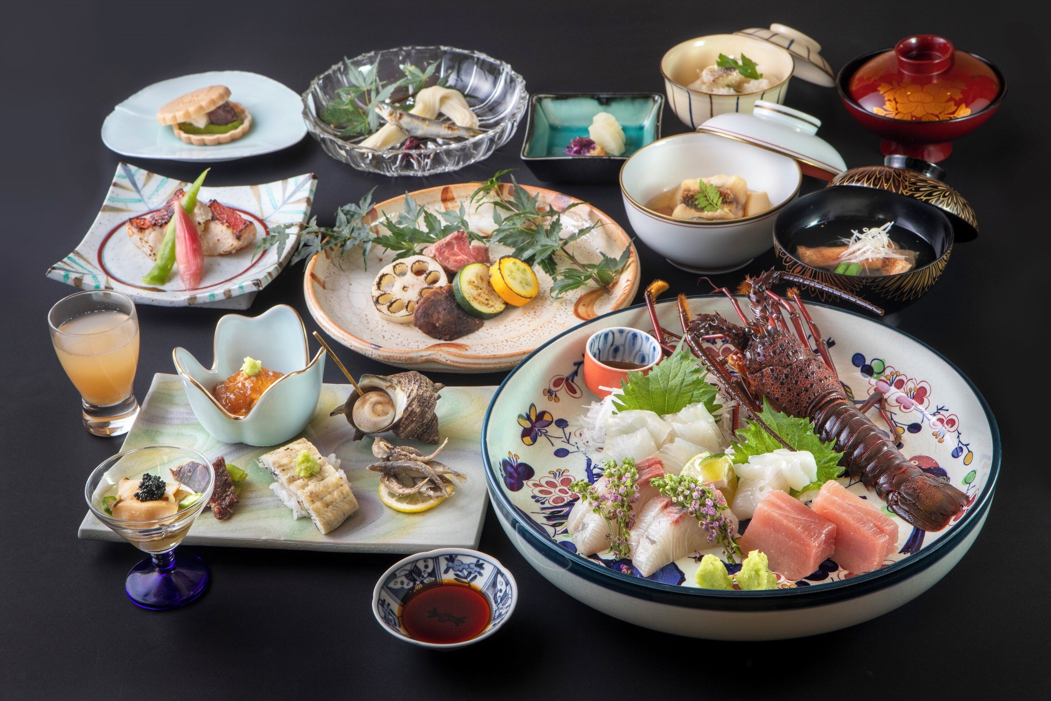A variety of dishes including sashimi, seafood, and a lobster, arranged on a table with multiple bowls and plates.