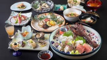 A variety of dishes including sashimi, seafood, and a lobster, arranged on a table with multiple bowls and plates.