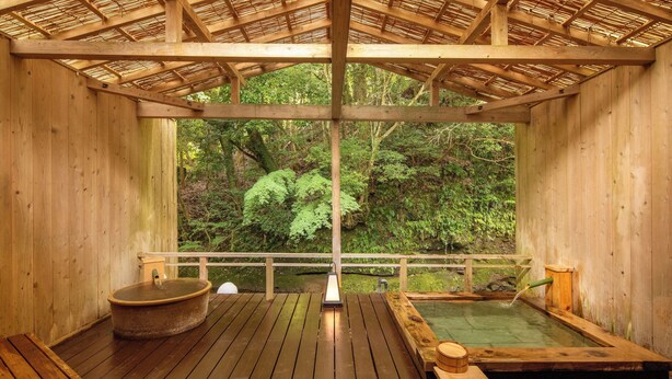 A wooden hot spring bath area with a wooden deck, benches, and a view of lush greenery. - MIZUMARI (Kawazu)