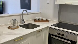 Een kleine keuken met een spoelbak, fornuis en koffiezetapparaat op het aanrecht.