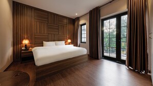 A modern hotel room with a large bed, wooden paneling, two bedside lamps, a view through a glass door, and a wooden floor.