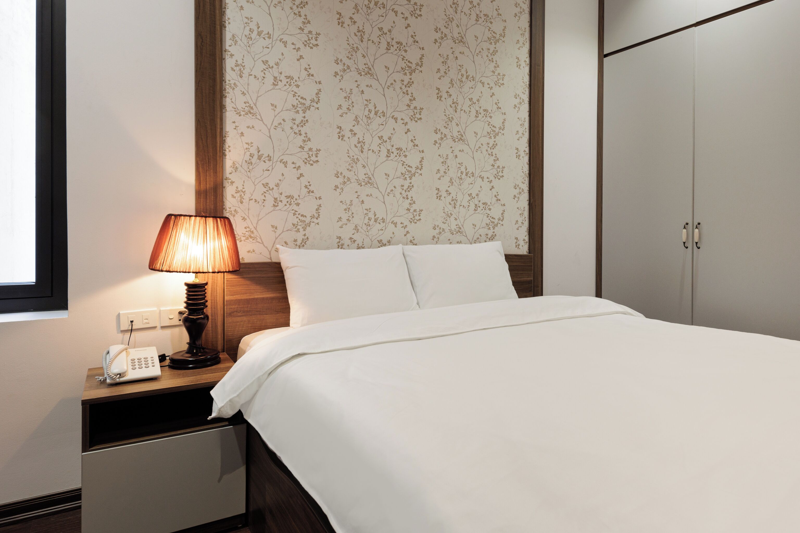 Een hotelkamer met een bed, een nachtkastje met lamp, een telefoon en een kledingkast.