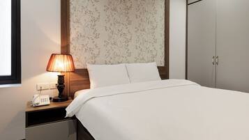 Een hotelkamer met een bed, een nachtkastje met lamp, een telefoon en een kledingkast.