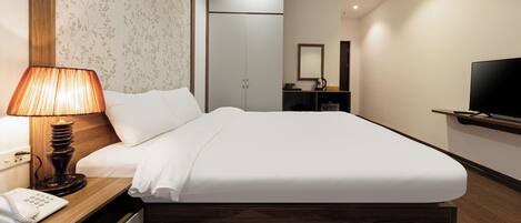 Habitación de hotel con una cama grande, una lámpara de noche, teléfono, armario, espejo, televisión y un escritorio pequeño con cafetera.