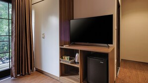 A modern room with a flat-screen TV, wooden shelving, a mini-fridge, and a sliding door closet.