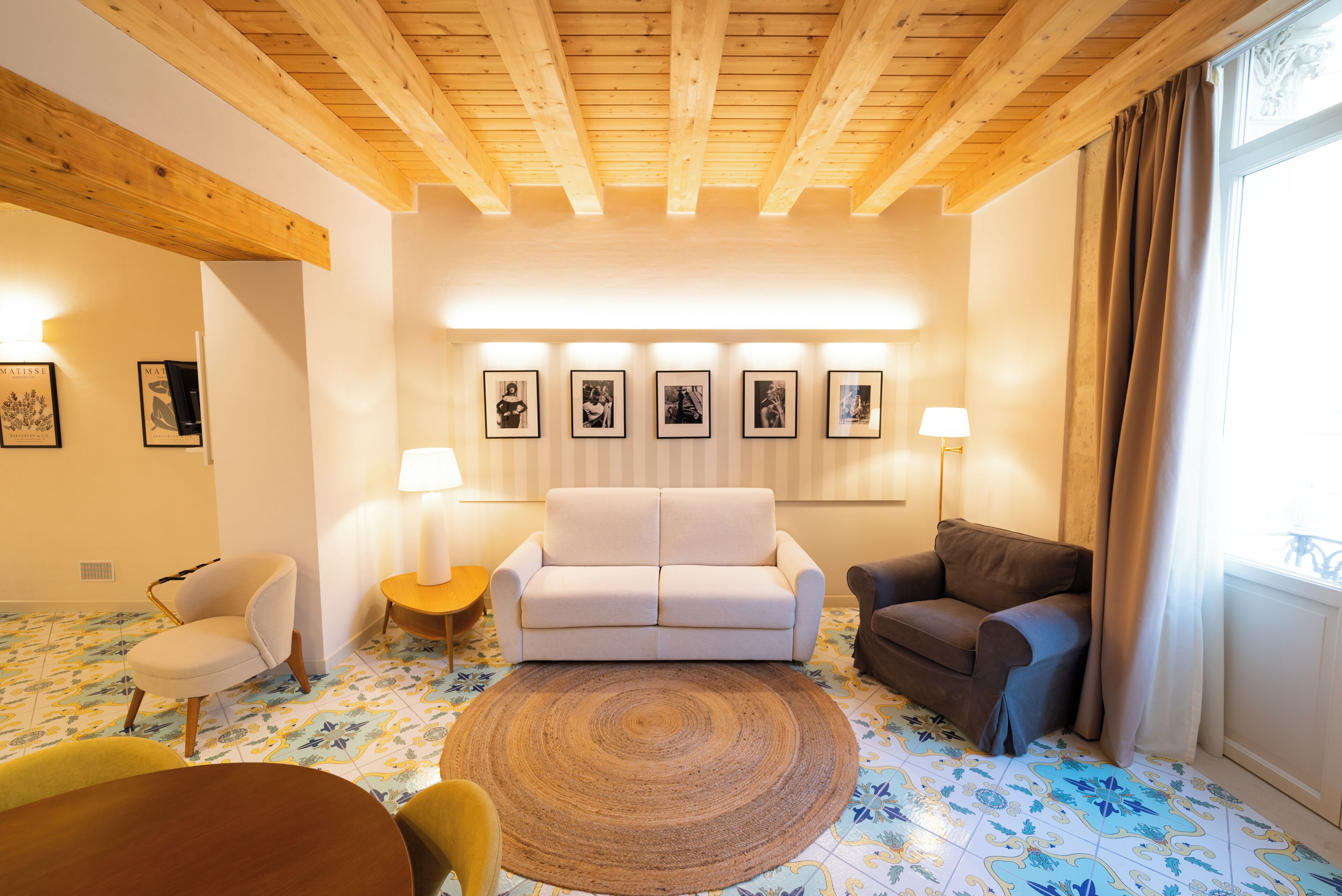 Una sala de estar con un sofá blanco, dos sillones, un tapete redondo y piso estampado.