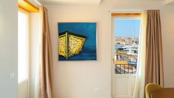 A room with a view of a marina, a painting on the wall, and a dining area.