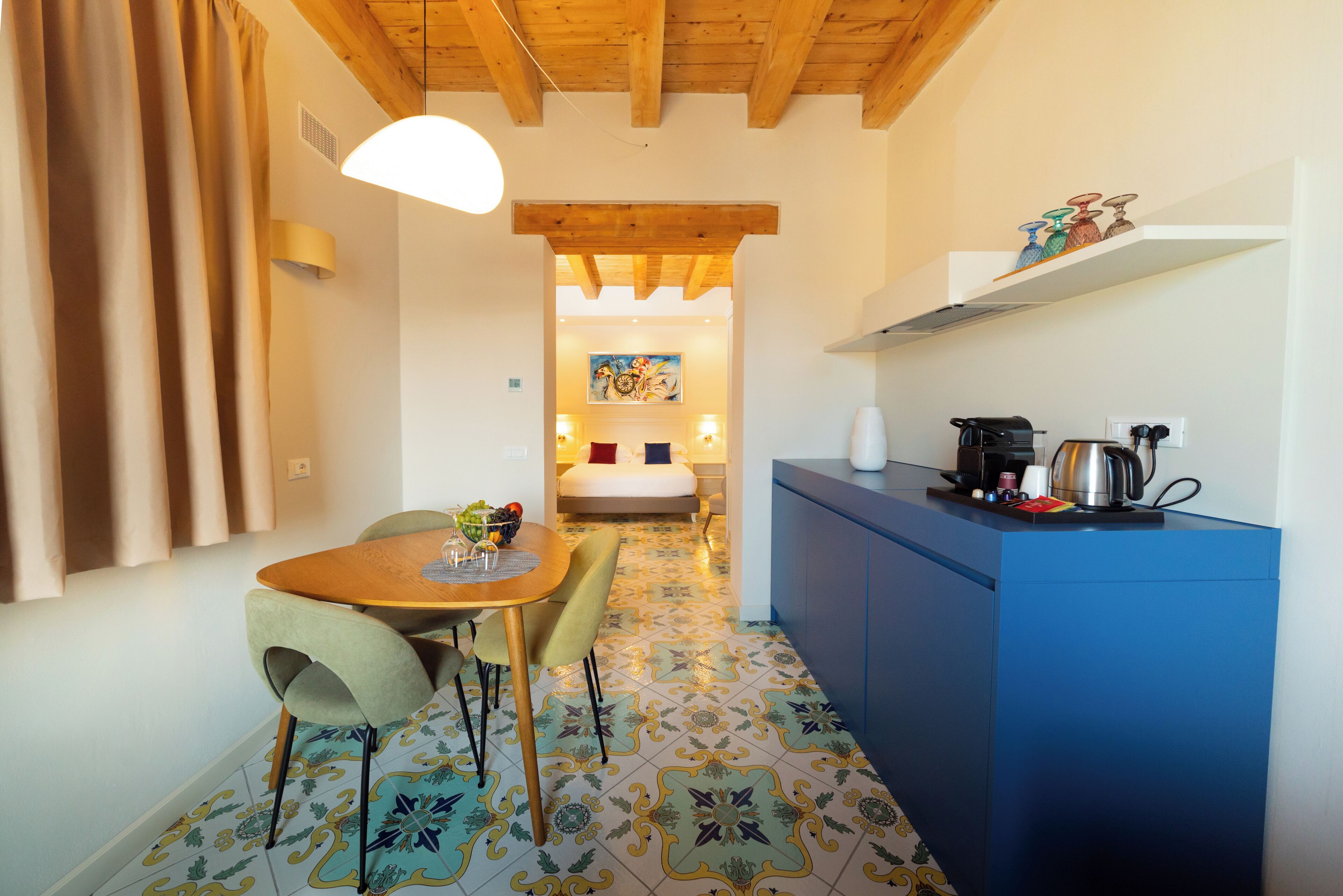A compact kitchen with a blue countertop, a dining area with a round table and chairs, and a patterned floor.