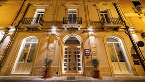 Um edifício histórico com entrada central, janelas em arco e uma varanda com grades de ferro.