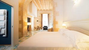 Quarto de hotel com uma cama grande, uma escrivaninha com cadeiras e vista através de um arco.