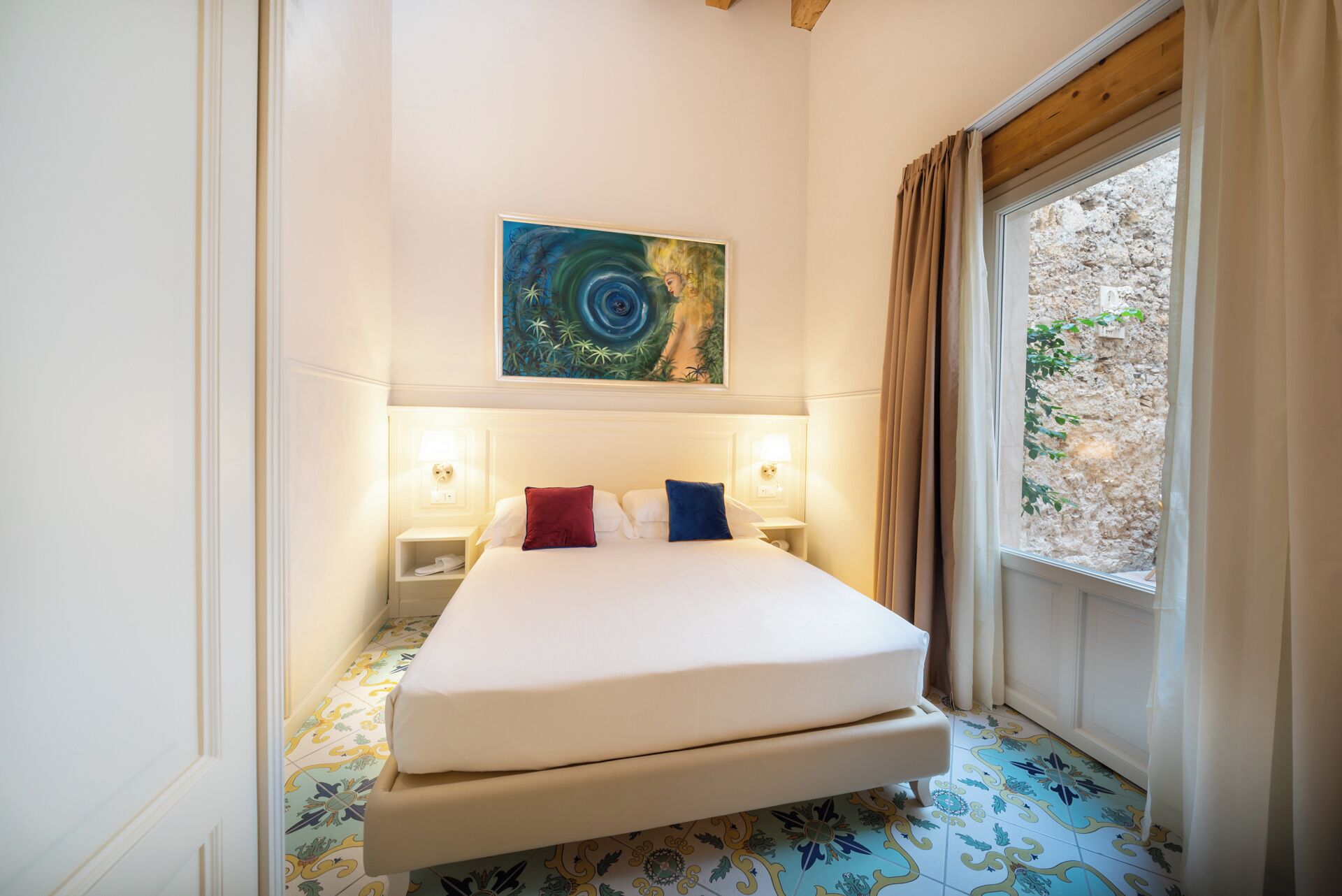 Une chambre d’hôtel avec un lit, deux lampes de chevet, un tableau au mur et une fenêtre avec des rideaux.