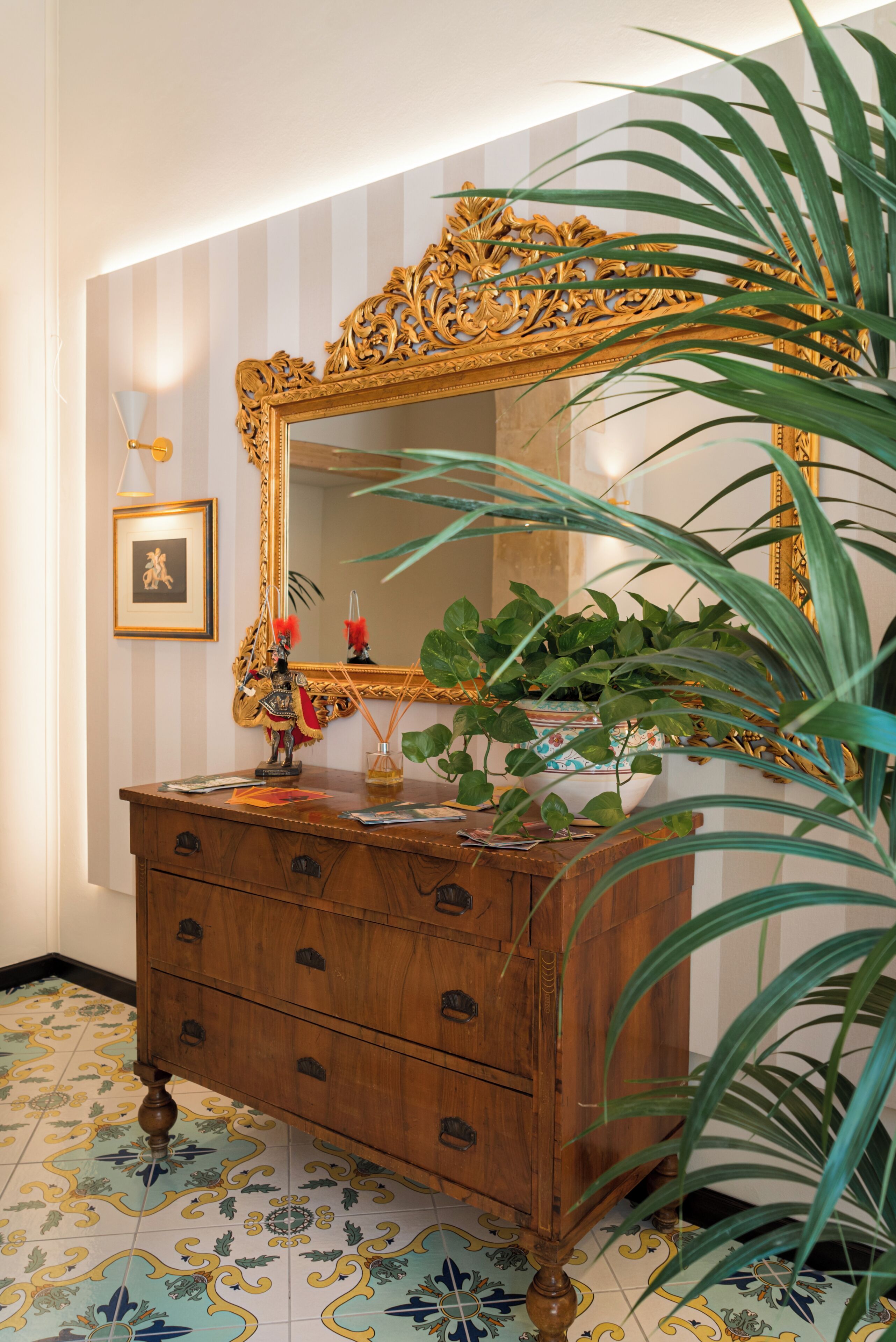 A wooden dresser with a large ornate mirror, a framed picture, and a potted plant.