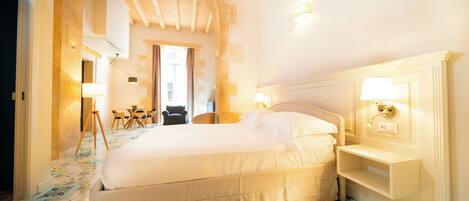 A hotel room with a large bed, a bedside table, a lamp, and a view of the hallway.