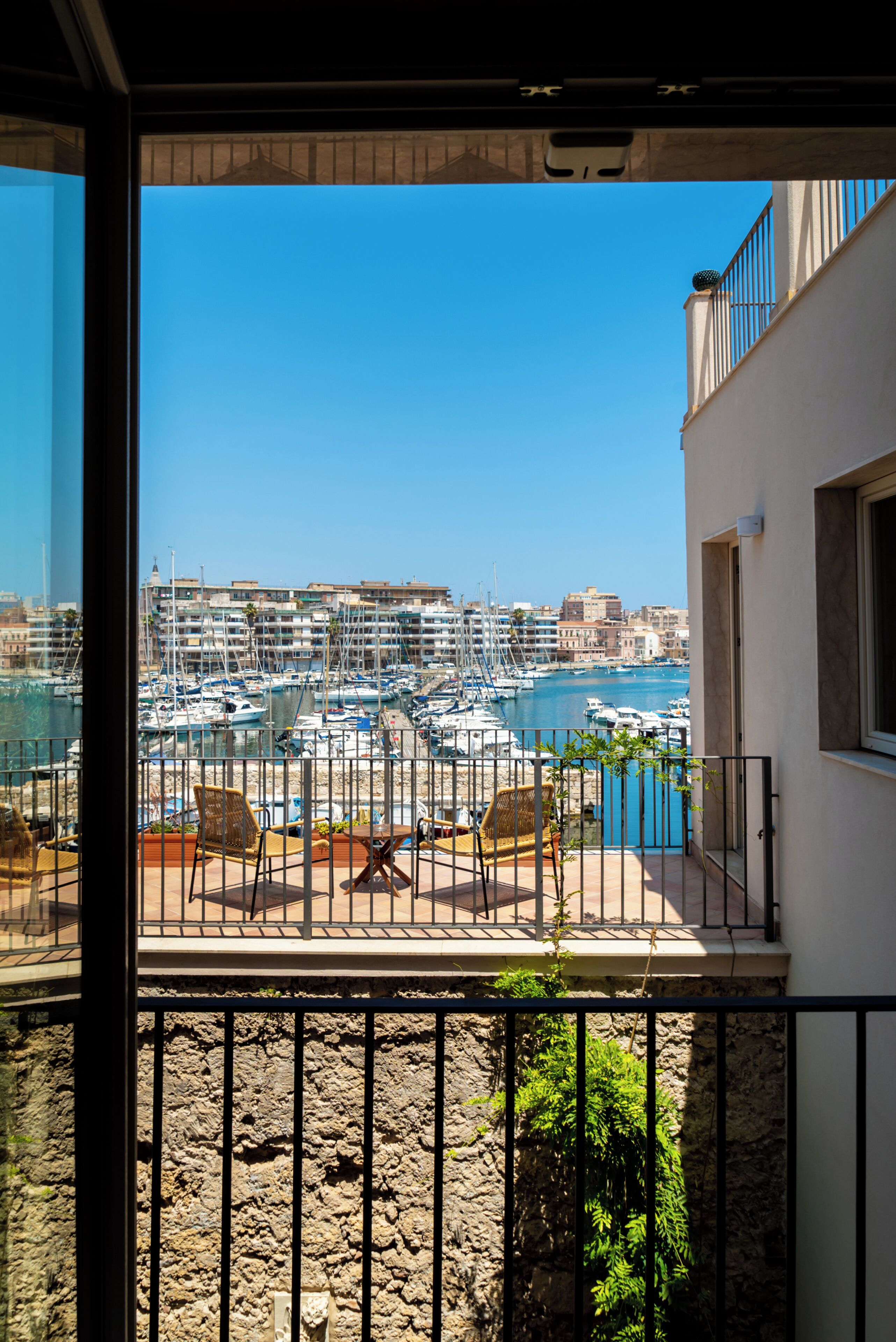 A balcony with a view of a marina, stone wall, and outdoor furniture.