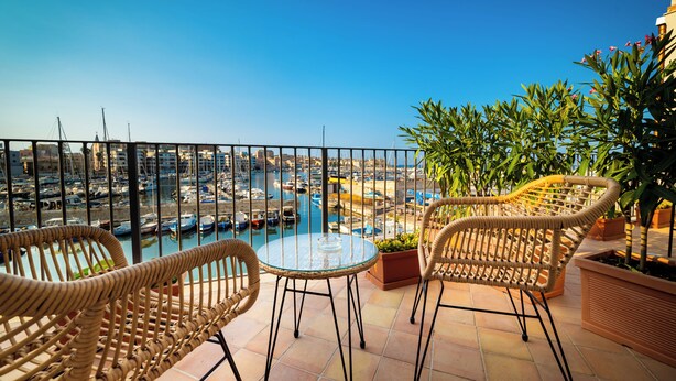 Varanda com cadeiras de vime e mesa de vidro com vista para uma marina e barcos.