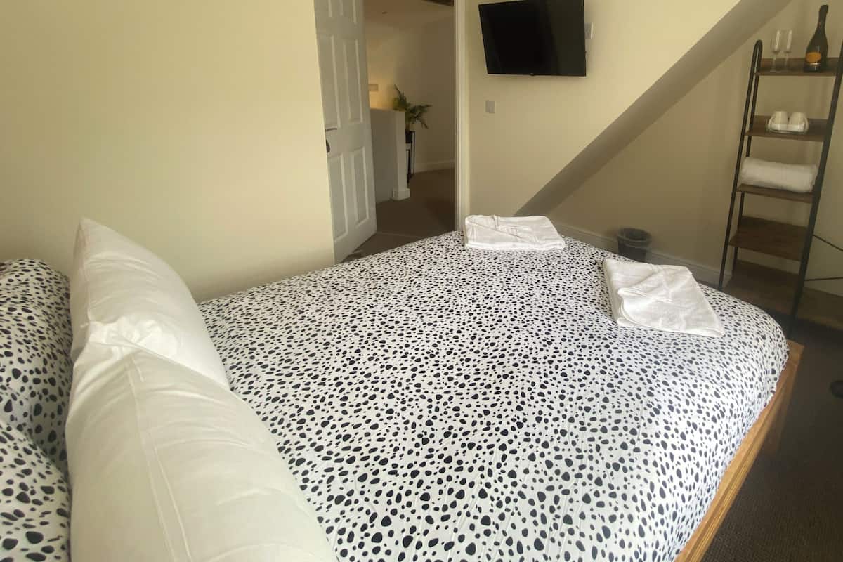 A bedroom with a bed, a TV mounted on the wall, and a staircase.