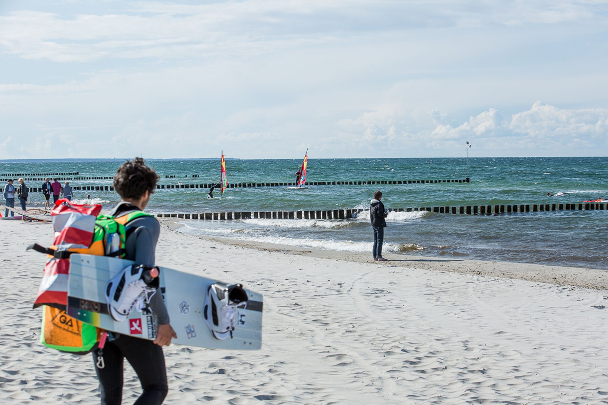 Une scène de plage où l’on voit une personne portant une planche de surf et un sac à dos.