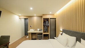 Una habitación de hotel con una cama, un escritorio con silla, un armario y una mesita de noche.