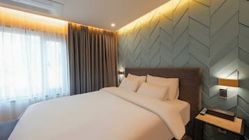 A hotel room with a large bed, a nightstand, a wall-mounted lamp, and a window with curtains.