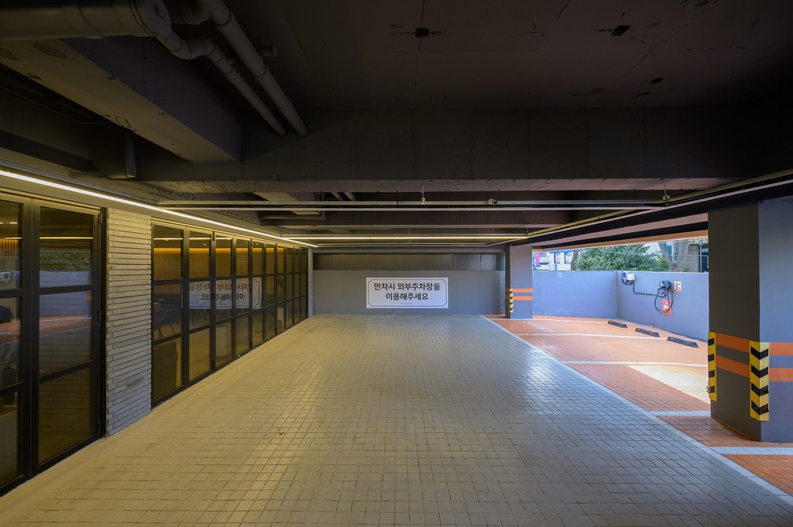 Un estacionamiento limpio y bien iluminado con suelo de baldosas, puertas de vidrio en un lado y un letrero en el centro.