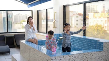 En modern inomhuspool med ett spaområde, stora fönster och utsikt över stadsbilden.