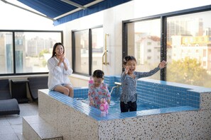 A modern indoor swimming pool with a spa area, large windows, and a view of the cityscape. - Mokpo H Avenue Hotel Peace Plaza (Mokpo)