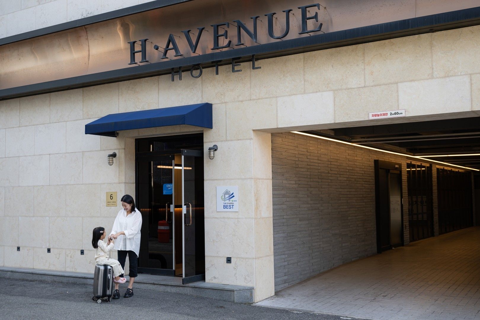 Entrada de hotel com uma placa indicando 'HAVENUE HOTEL' e um toldo azul.