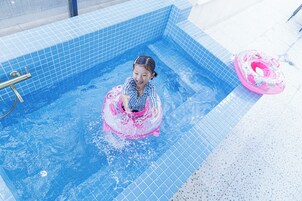 Niño en una piscina con un círculo inflable rosa, rodeado de paredes de azulejos azules.
