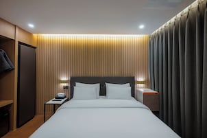 Una habitación de hotel con una cama, mesitas de noche, un armario y una cortina.