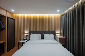 Una habitación de hotel con una cama, mesitas de noche, un armario y una cortina.