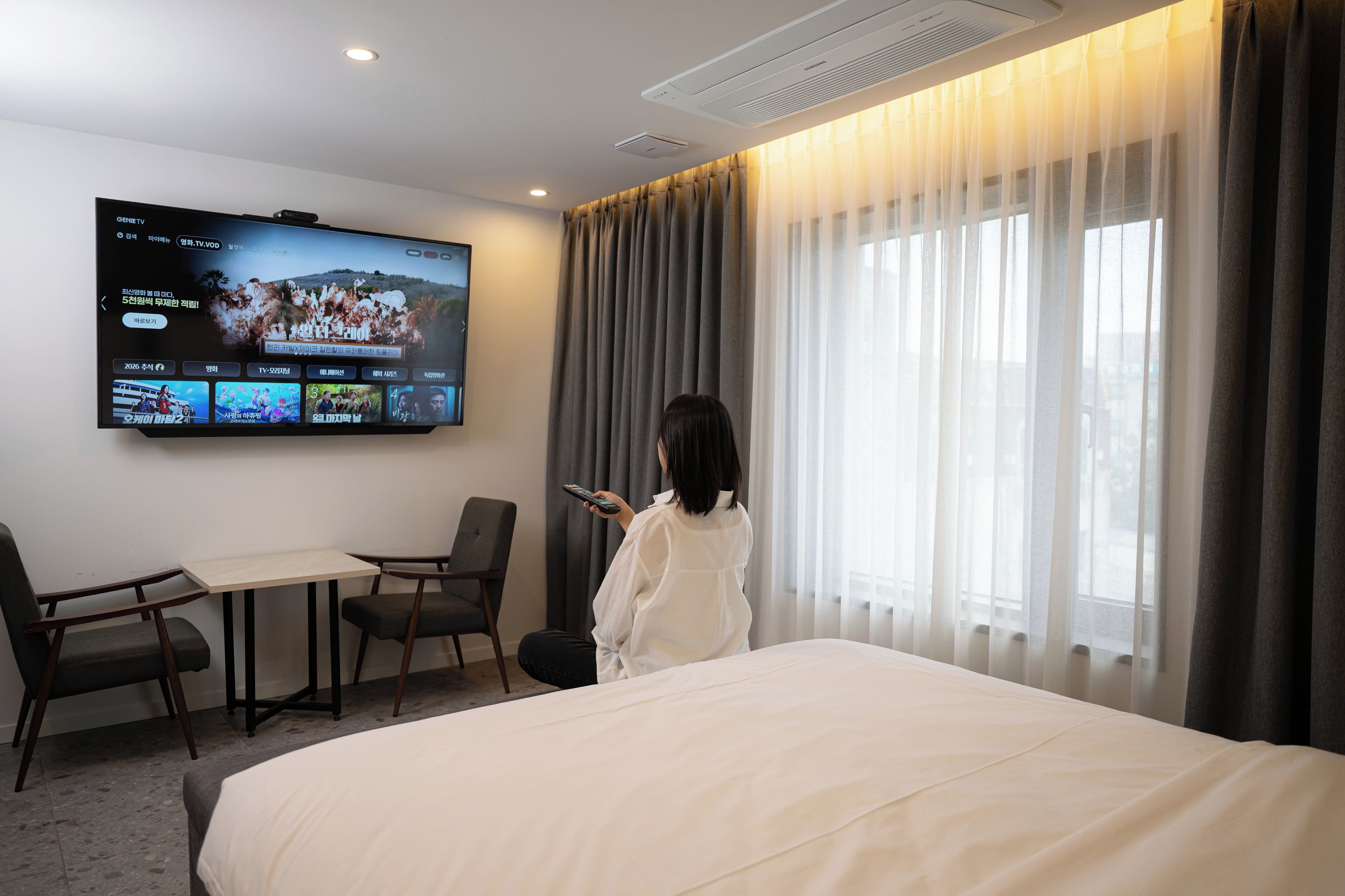 Habitación de hotel con una cama, un televisor montado en la pared, una mesa y dos sillas.