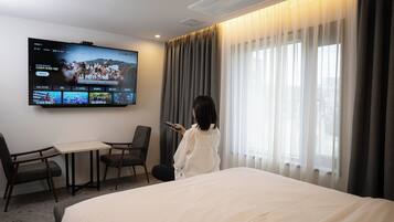 Habitación de hotel con una cama, un televisor montado en la pared, una mesa y dos sillas.